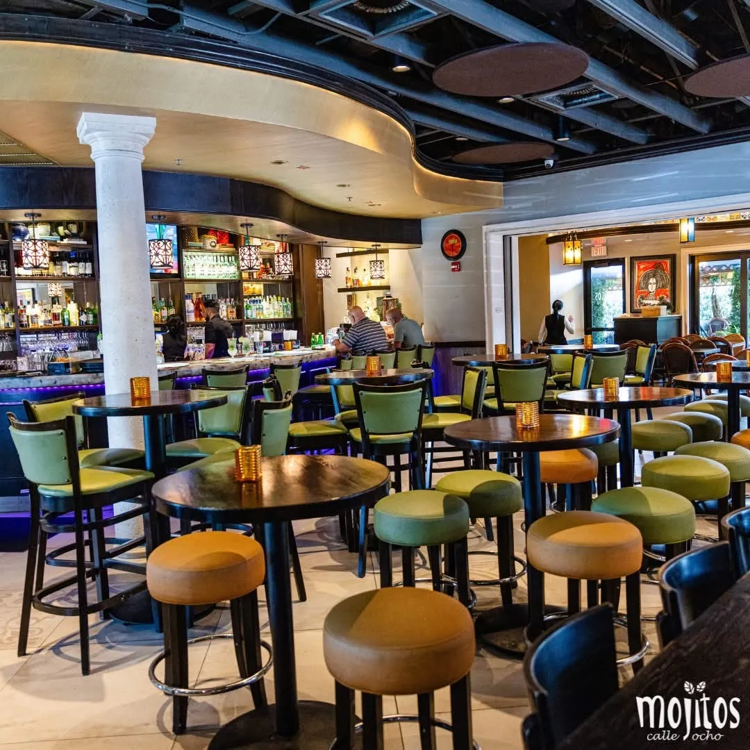 Bar lounge with high-top tables, green and mustard stools and a stocked back bar at Mojitos Calle 8 Cuban restaurant, Miami