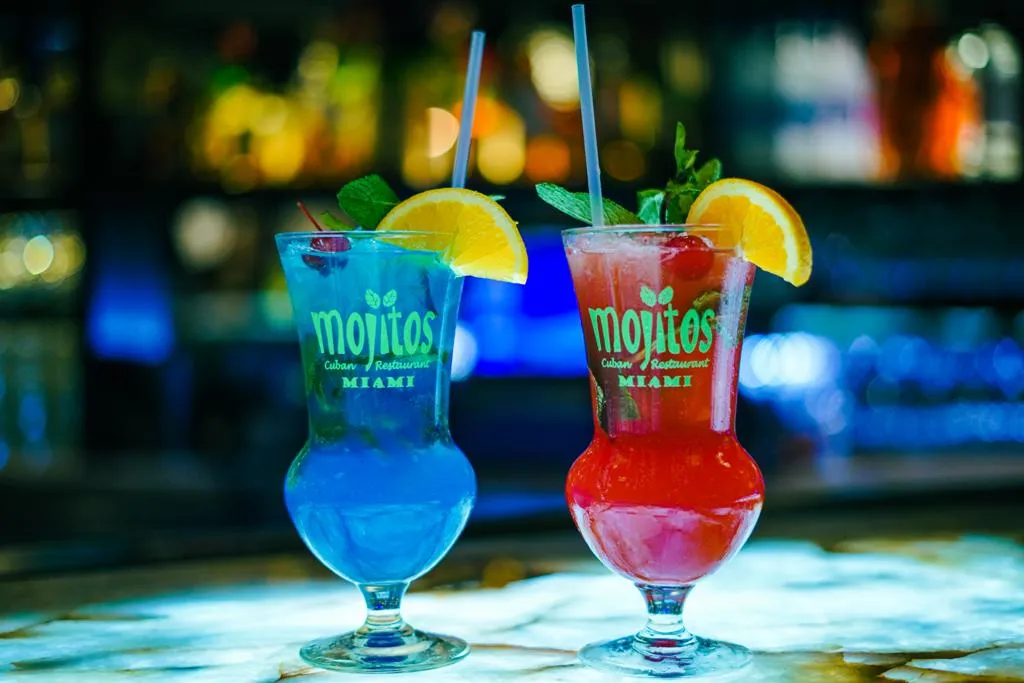 Mojitos azul y rojo en copas huracán de la casa con menta, rodaja de naranja y cereza en Mojitos Calle 8, restaurante cubano en Miami