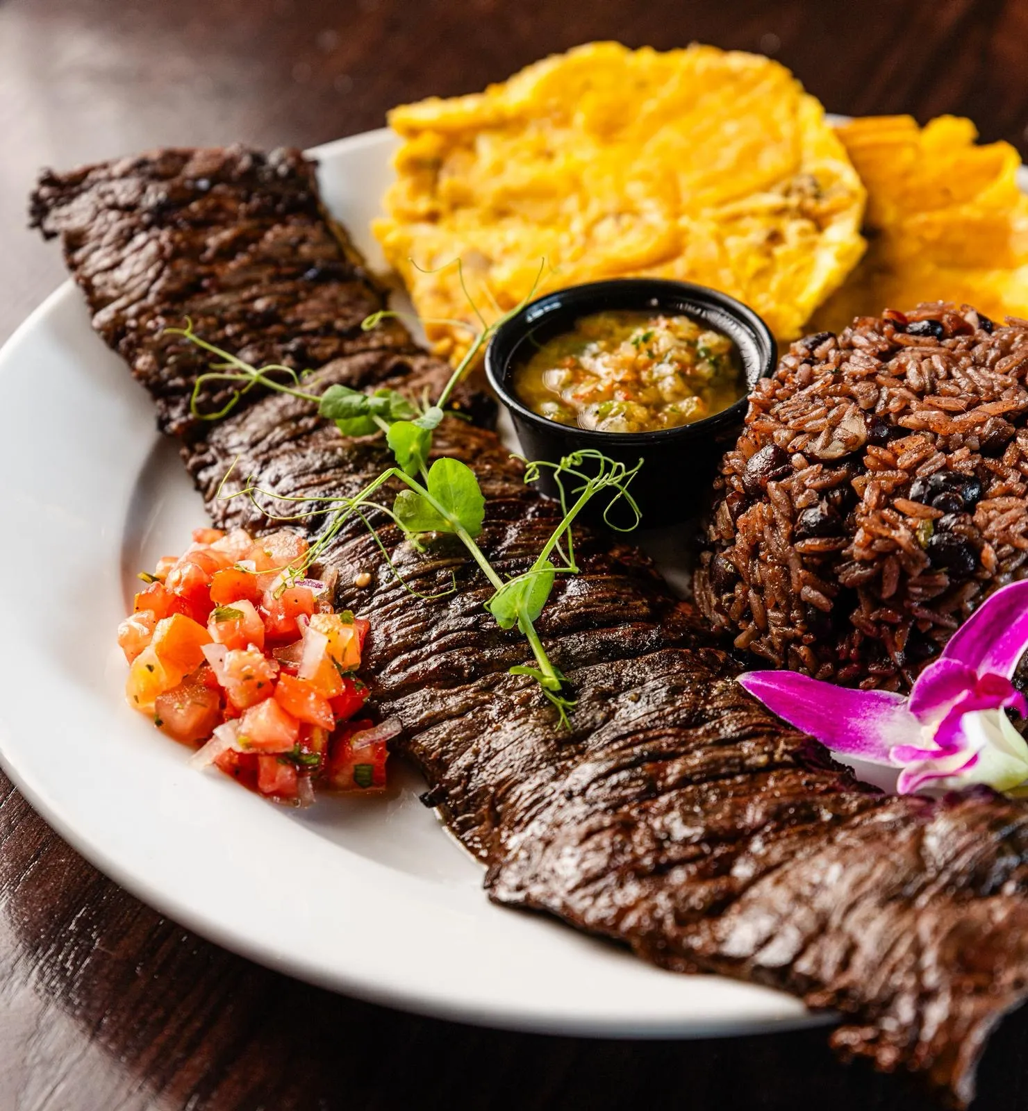 Churrasco a la parrilla servido con congrí, tostones dorados, chimichurri y salsa fresca de tomate en Mojitos Calle 8, restaurante cubano en Miami