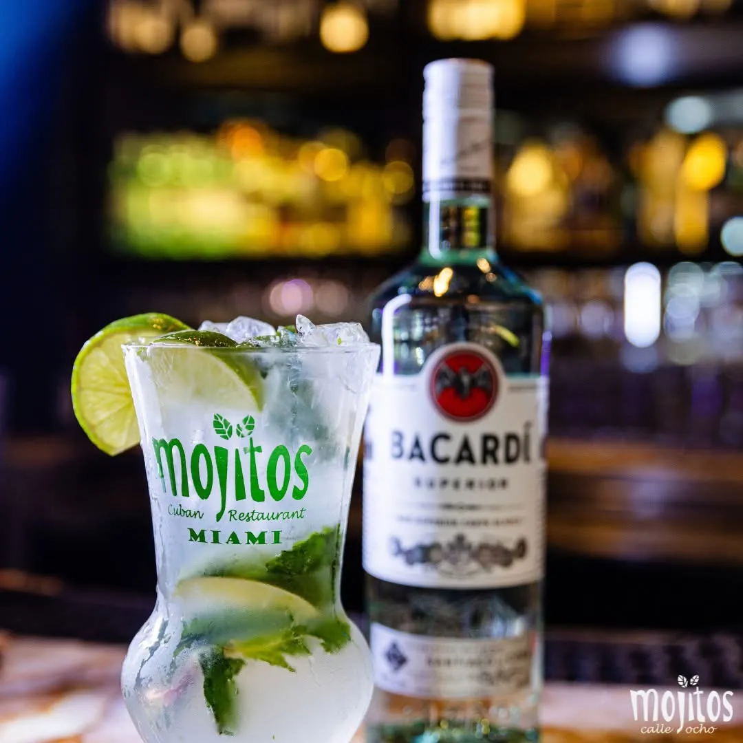 Mojito clásico con ruedas de limón y menta macerada sobre hielo frapé junto a una botella de ron blanco Bacardi Superior en Mojitos Calle 8, restaurante cubano en Miami