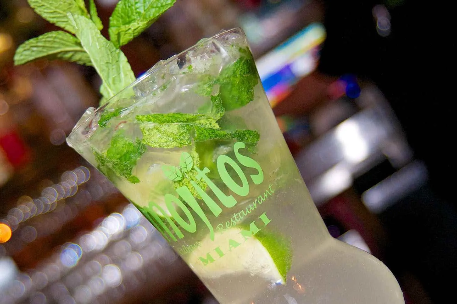 Mojito clásico inclinado repleto de hojas de menta fresca y limón sobre hielo bajo las luces del bar en Mojitos Calle 8, restaurante cubano en Miami