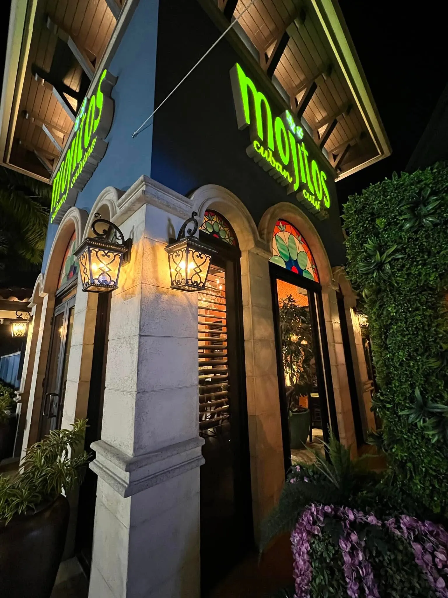 Corner entrance at night with iron lanterns, stone arches and colorful stained-glass windows at Mojitos Calle 8 on Calle Ocho, Miami