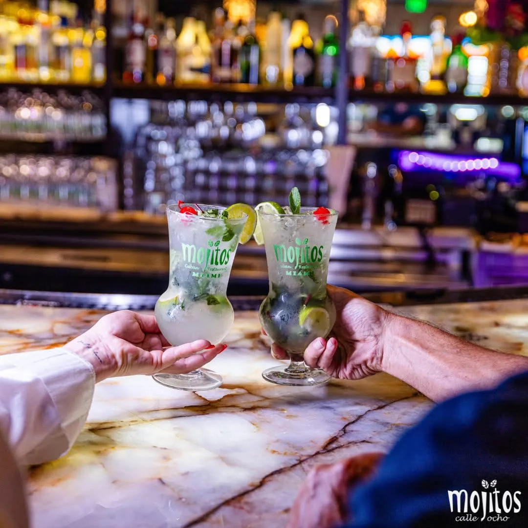 Pareja brindando con dos mojitos clásicos con limón y menta sobre la barra de mármol en Mojitos Calle 8, restaurante cubano en Miami