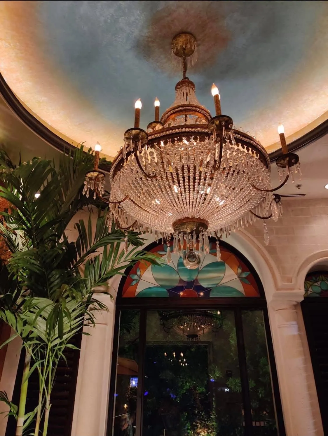 Crystal chandelier hanging from the painted domed ceiling above a stained-glass arch at Mojitos Calle 8, Miami