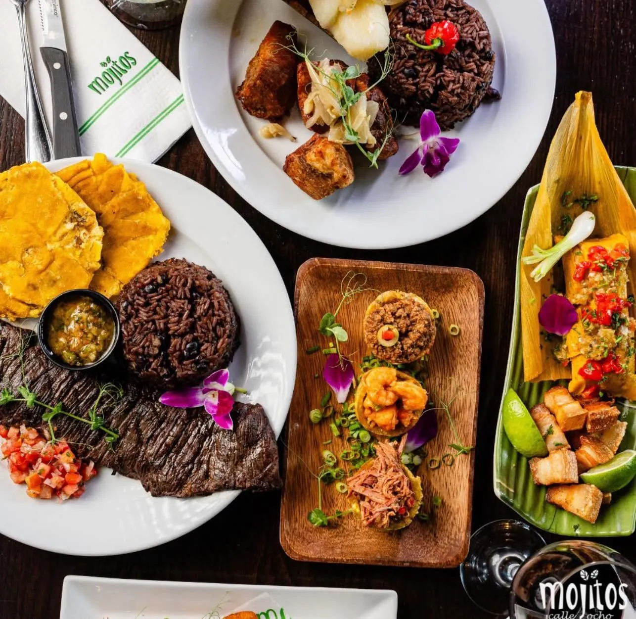 Vista aérea de platos cubanos: churrasco con congrí y tostones, masas de puerco con moros, tostones rellenos de camarón y picadillo, un tamal y chicharrones crujientes en Mojitos Calle 8 en Miami