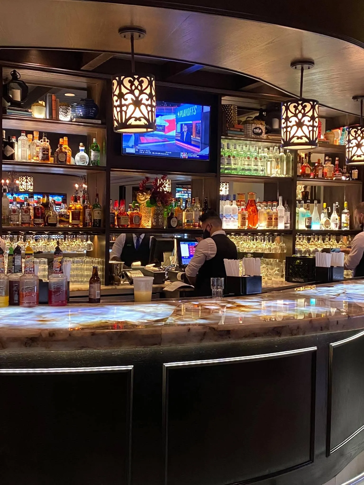Curved backlit onyx bar with tall liquor shelves, pendant lamps and bartenders at work, Mojitos Calle 8 Cuban restaurant Miami