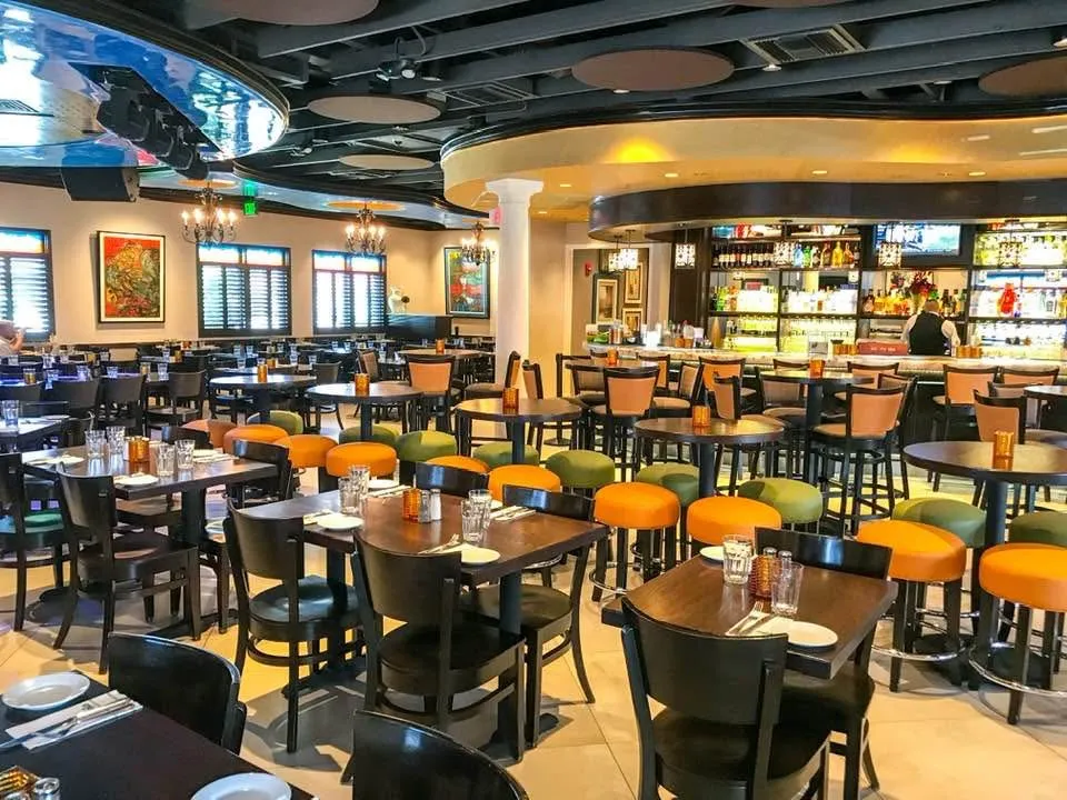 Empty dining room with orange and green bar stools, colorful artwork and the full bar at Mojitos Calle 8, Cuban restaurant in Miami