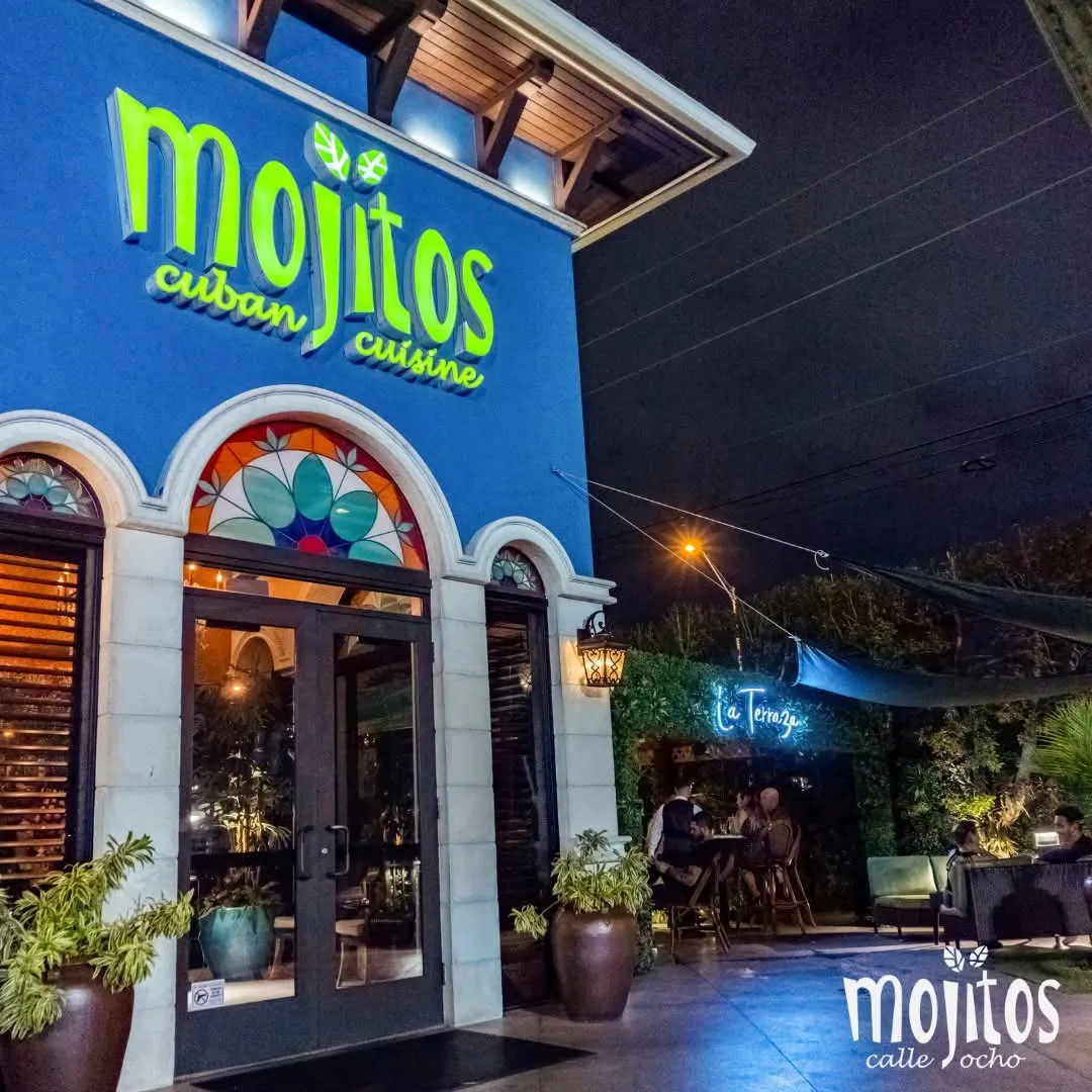 Entrance doors beside the La Terraza neon sign and outdoor seating with guests at Mojitos Calle 8, Cuban restaurant in Miami