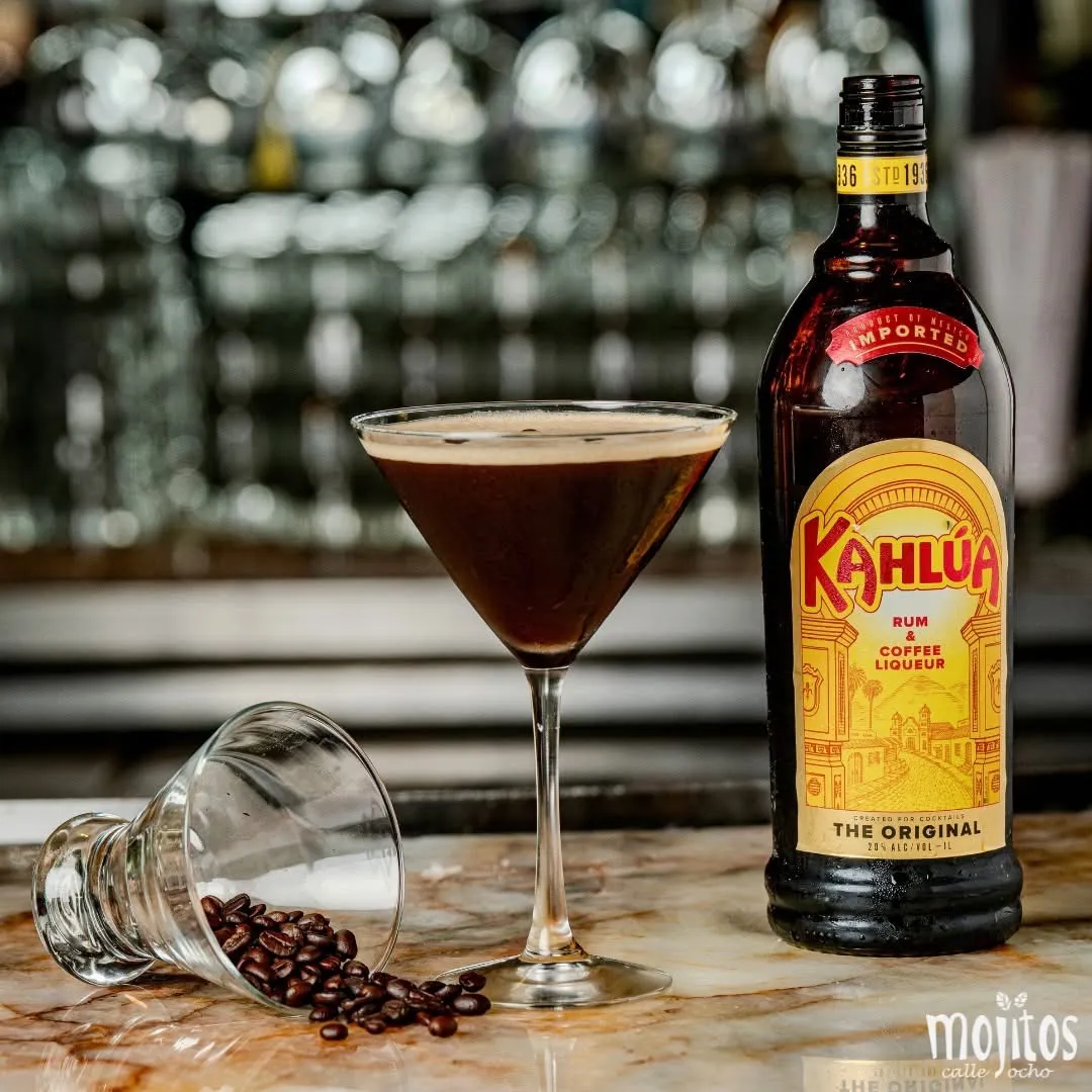 Espresso martini con espuma cremosa junto a una botella de Kahlúa y granos de café derramados sobre la barra de mármol en Mojitos Calle 8, restaurante cubano en Miami