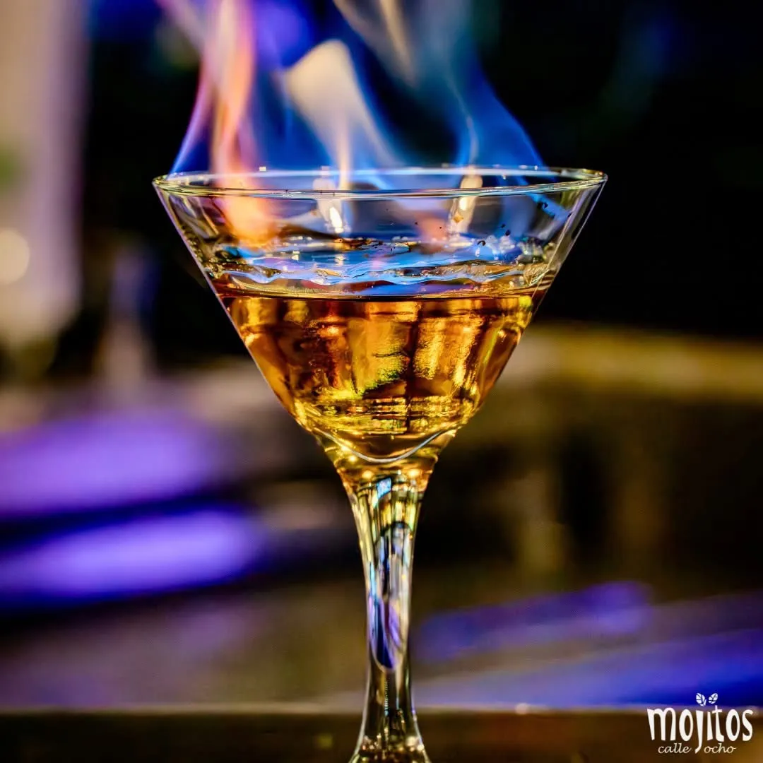 Martini flameado con llamas azules bailando sobre el licor dorado en una copa en Mojitos Calle 8, restaurante cubano en Miami