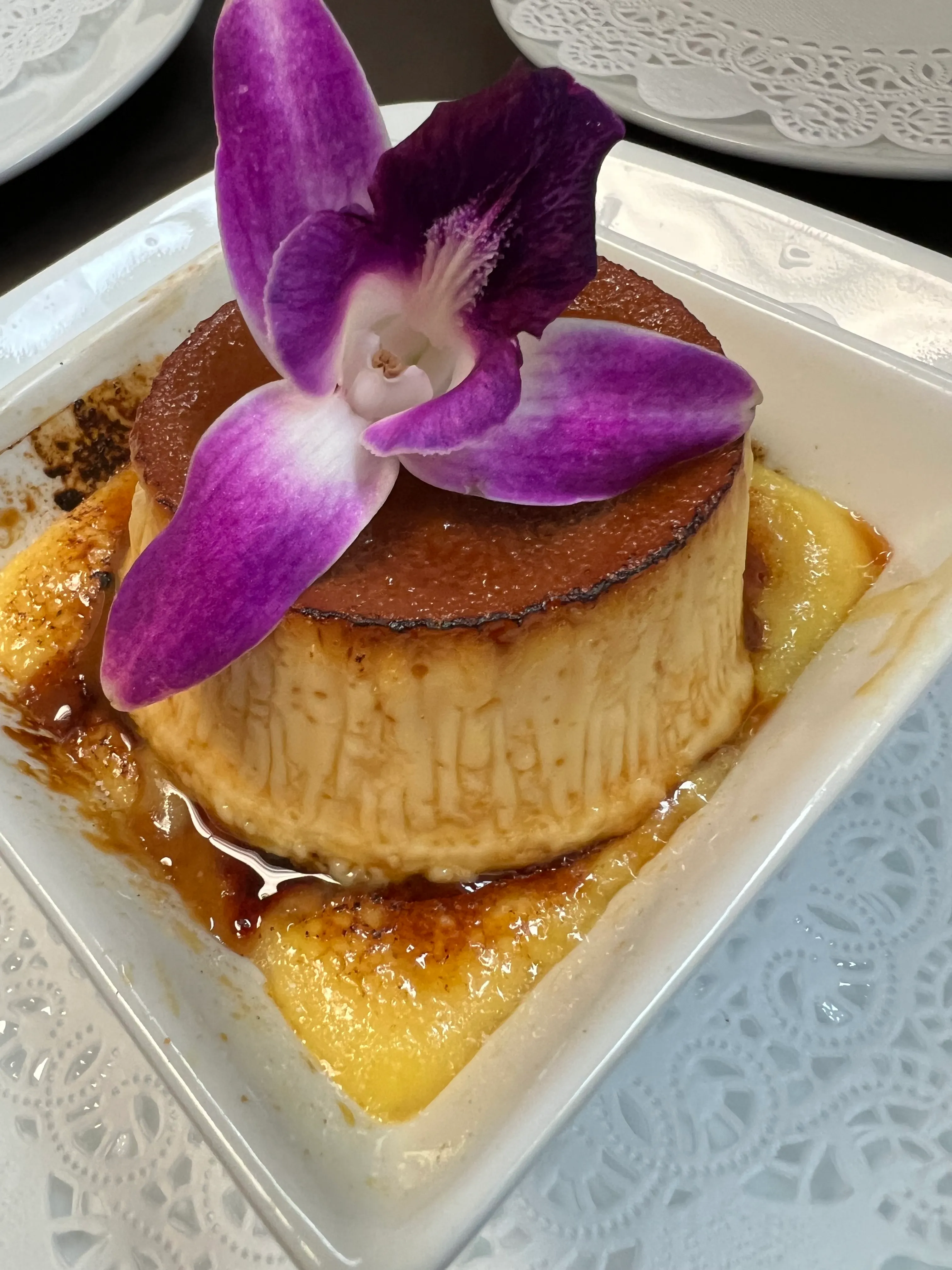 Porción de flan de queso cubano con salsa de caramelo y una orquídea morada como decoración en Mojitos Calle 8, restaurante cubano en Miami