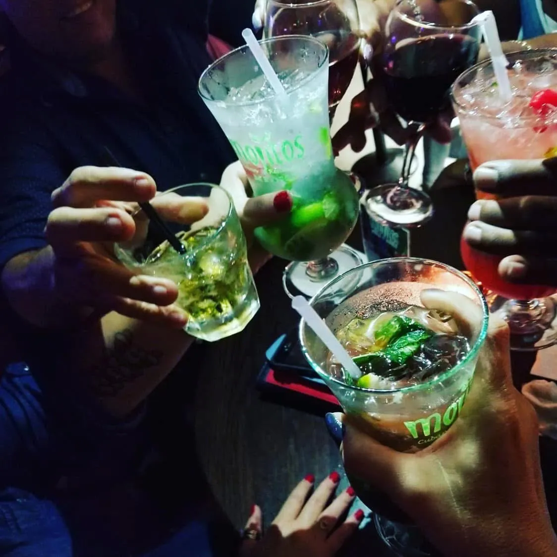 Grupo de amigos levantando mojitos, sangría y cócteles rosados juntos en una noche en Mojitos Calle 8, restaurante cubano en Miami