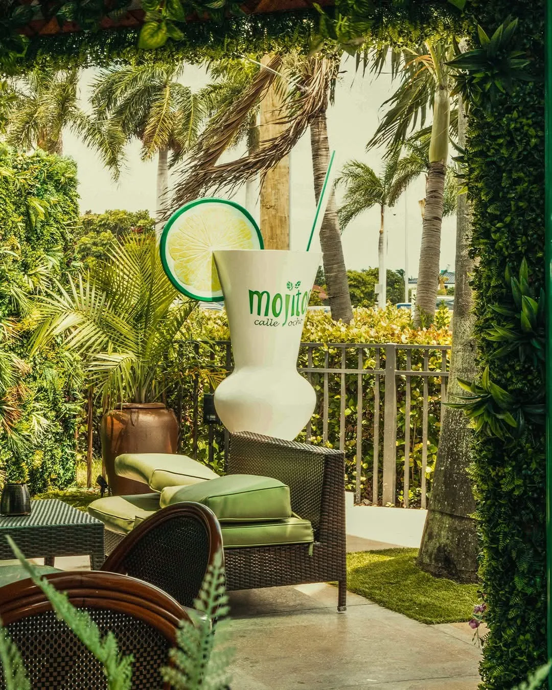 Giant mojito glass sculpture with lime slice among palms and greenery on the terrace at Mojitos Calle 8, Miami