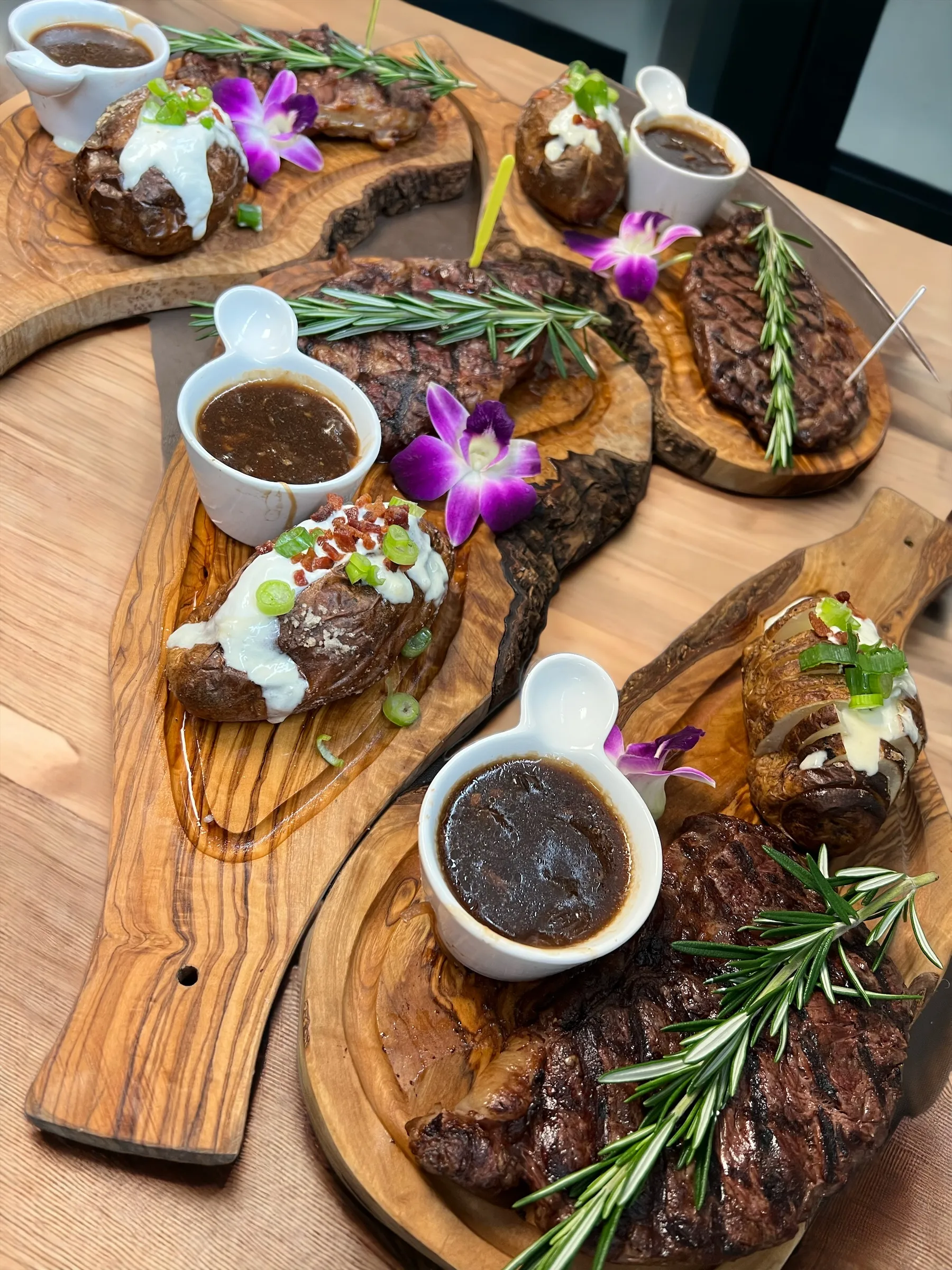 Varios bistecs a la parrilla servidos en tablas de madera de olivo con papas asadas rellenas, salsa de champiñones y romero en Mojitos Calle 8, restaurante cubano en Miami