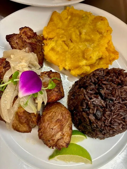 Masas de puerco fritas cubanas con cebolla encurtida, servidas con congrí, tostones y un gajo de limón en Mojitos Calle 8 en Miami