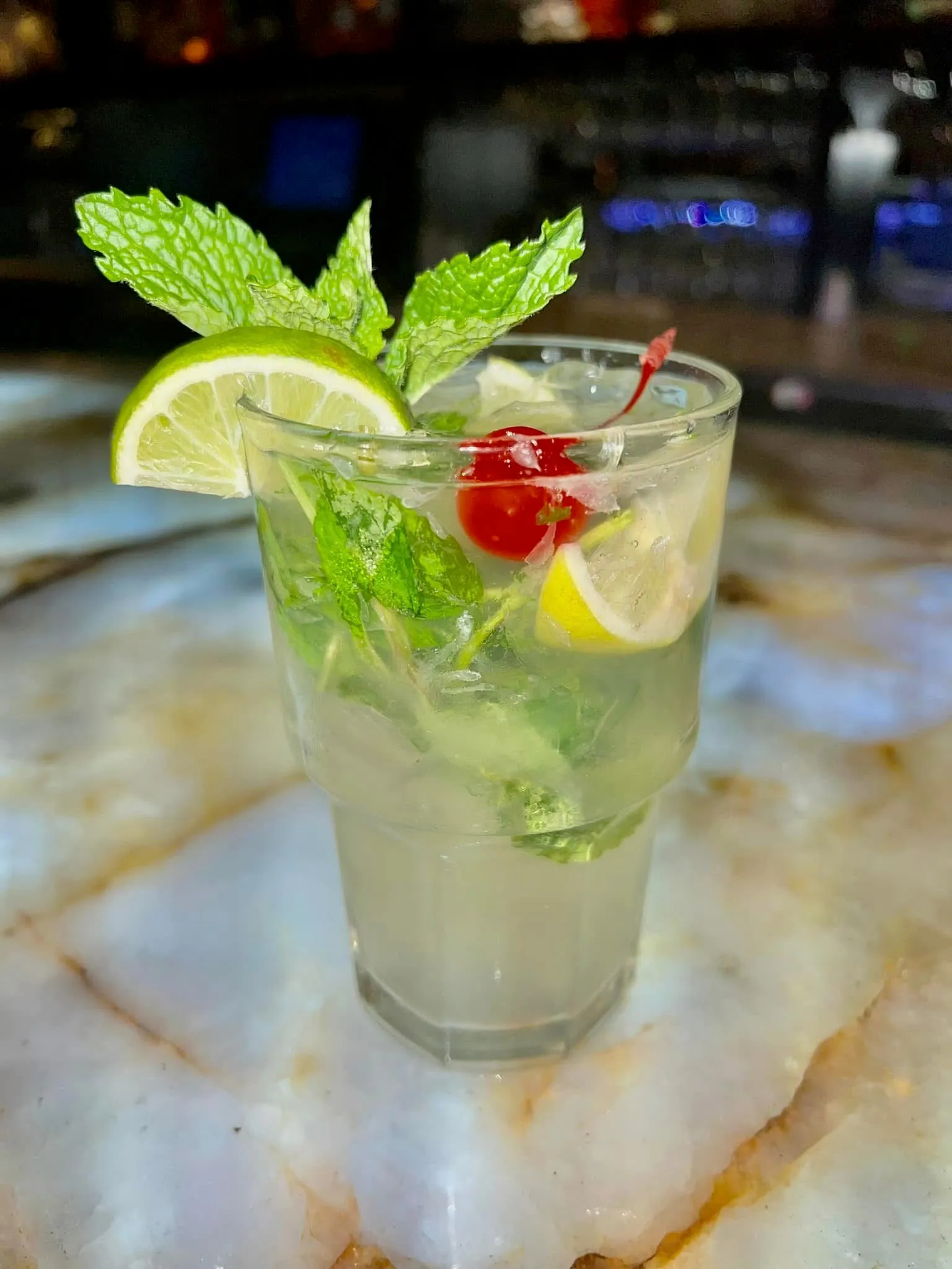 Mojito individual en vaso bajo con gajo de limón, ramitas de menta fresca y una cereza sobre la barra de ónix en Mojitos Calle 8, restaurante cubano en Miami