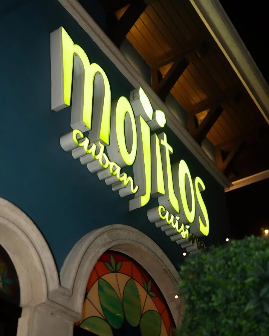 Close-up of the glowing neon-green Mojitos Cuban Cuisine lettering above the arched stained-glass window on Calle Ocho, Miami