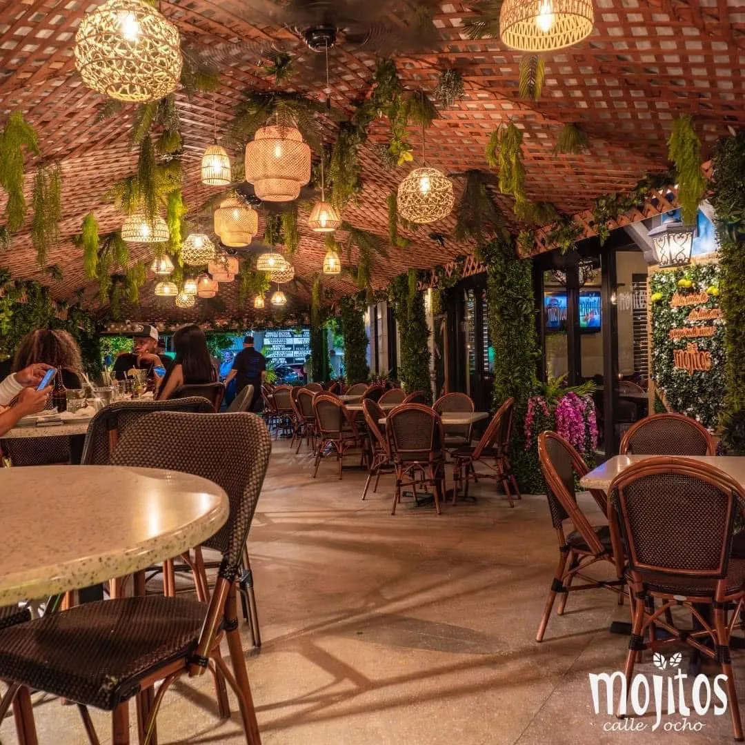 Open-air terraza with woven rattan lanterns, hanging greenery and bistro chairs at Mojitos Calle 8, Cuban restaurant in Miami