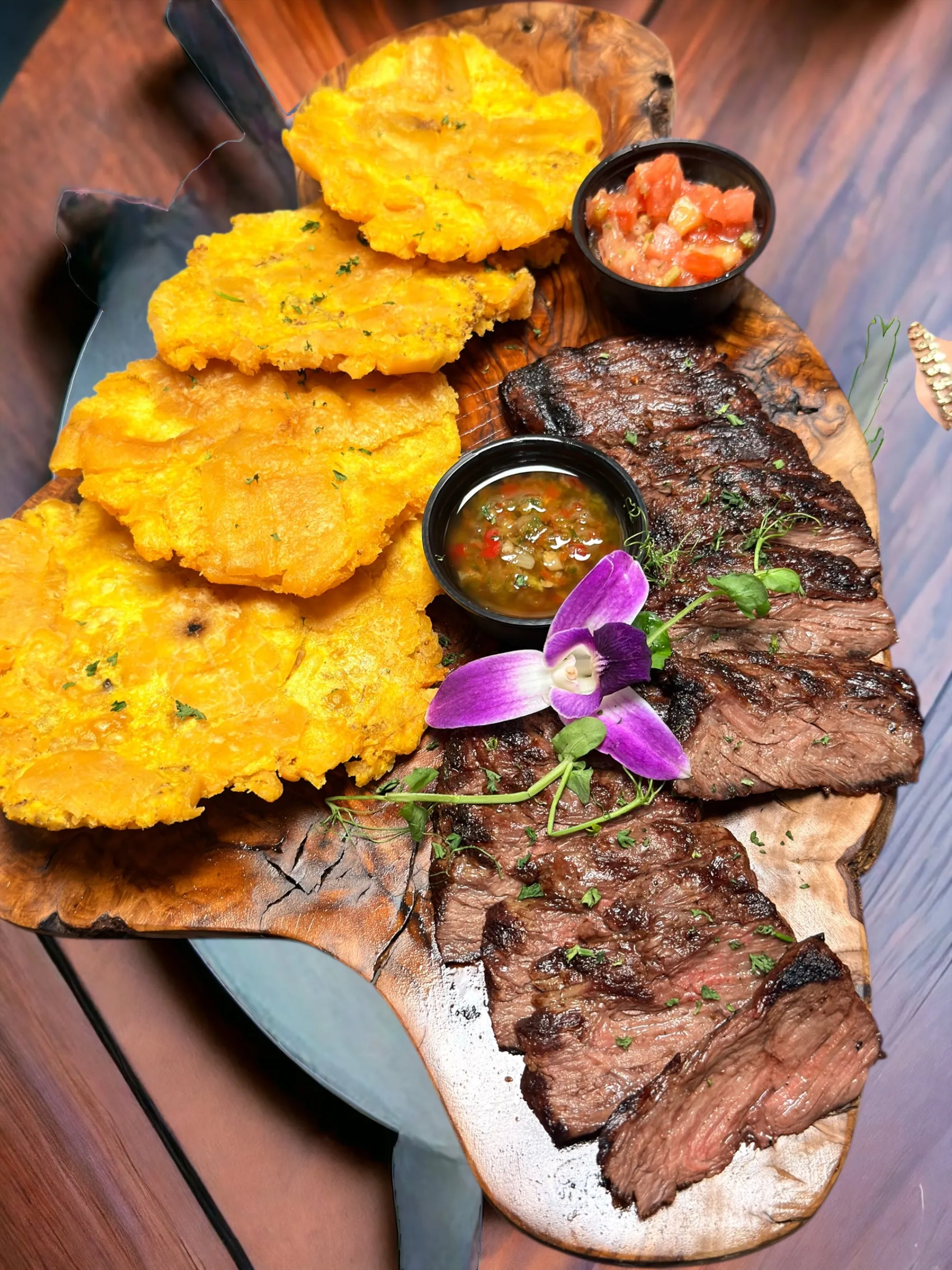 Churrasco a la parrilla en rodajas sobre tabla de madera con una torre de tostones crujientes, chimichurri y salsa de tomate en Mojitos Calle 8, restaurante cubano en Miami
