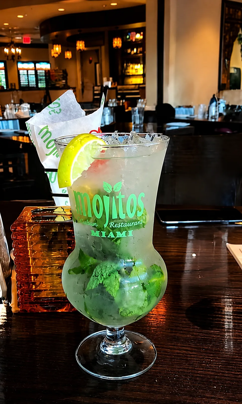Mojito tradicional en copa huracán de la casa con hielo frapé, menta y rueda de limón sobre mesa de madera en el comedor de Mojitos Calle 8, restaurante cubano en Miami