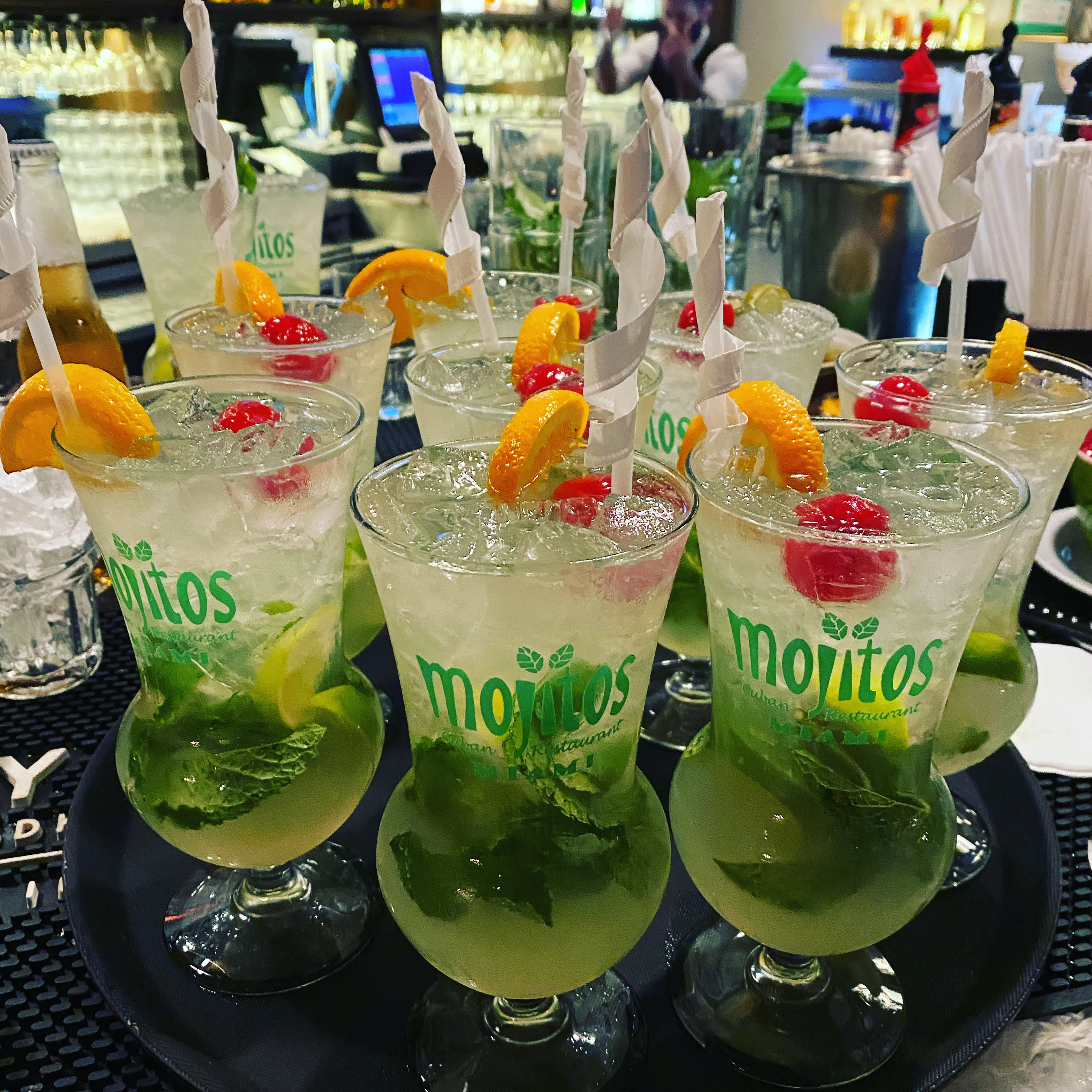 Bandeja de bar llena de mojitos cubanos clásicos con hielo frapé, menta macerada y limón, decorados con naranja y cereza en Mojitos Calle 8 en Miami