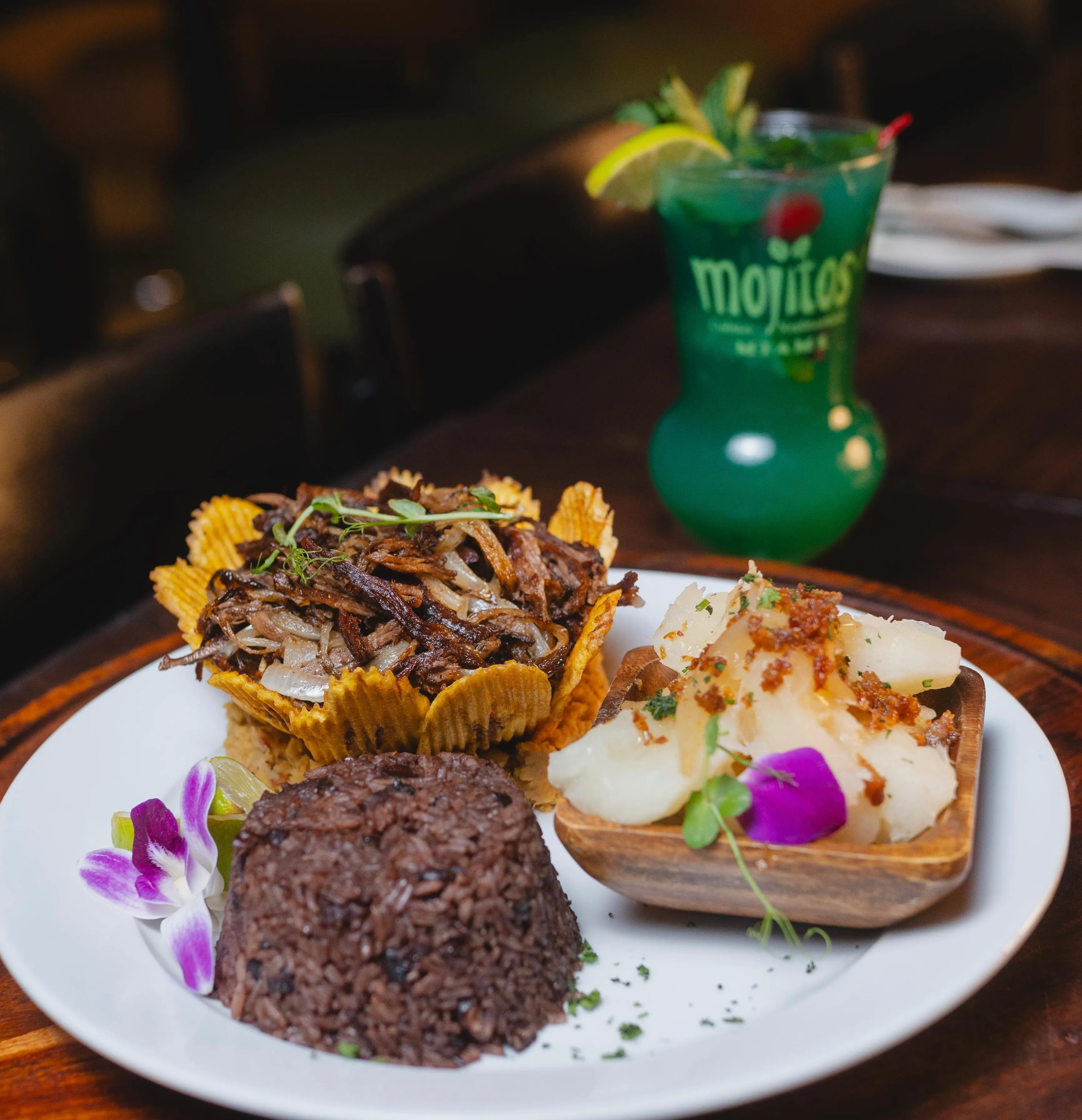 Vaca frita crujiente en canasta de plátano servida con congrí y yuca hervida con mojo, junto a un cóctel de la casa, en Mojitos Calle 8 en Miami